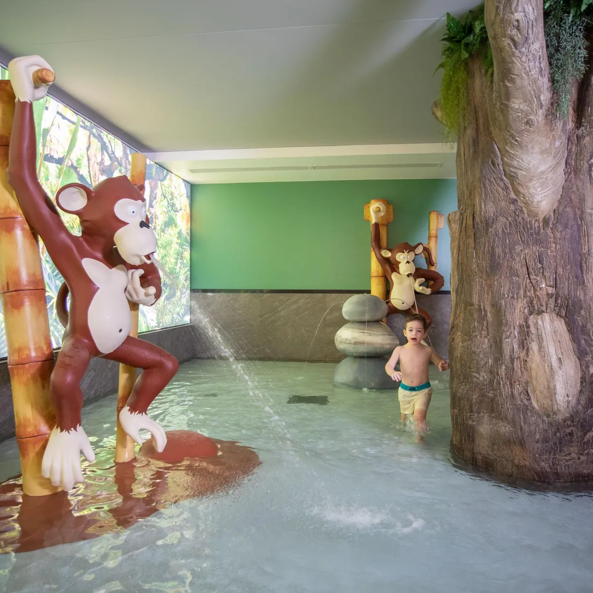 Un enfant joue dans une piscine pour enfants à thème jungle avec des sculptures de singes et des arbres en décoration