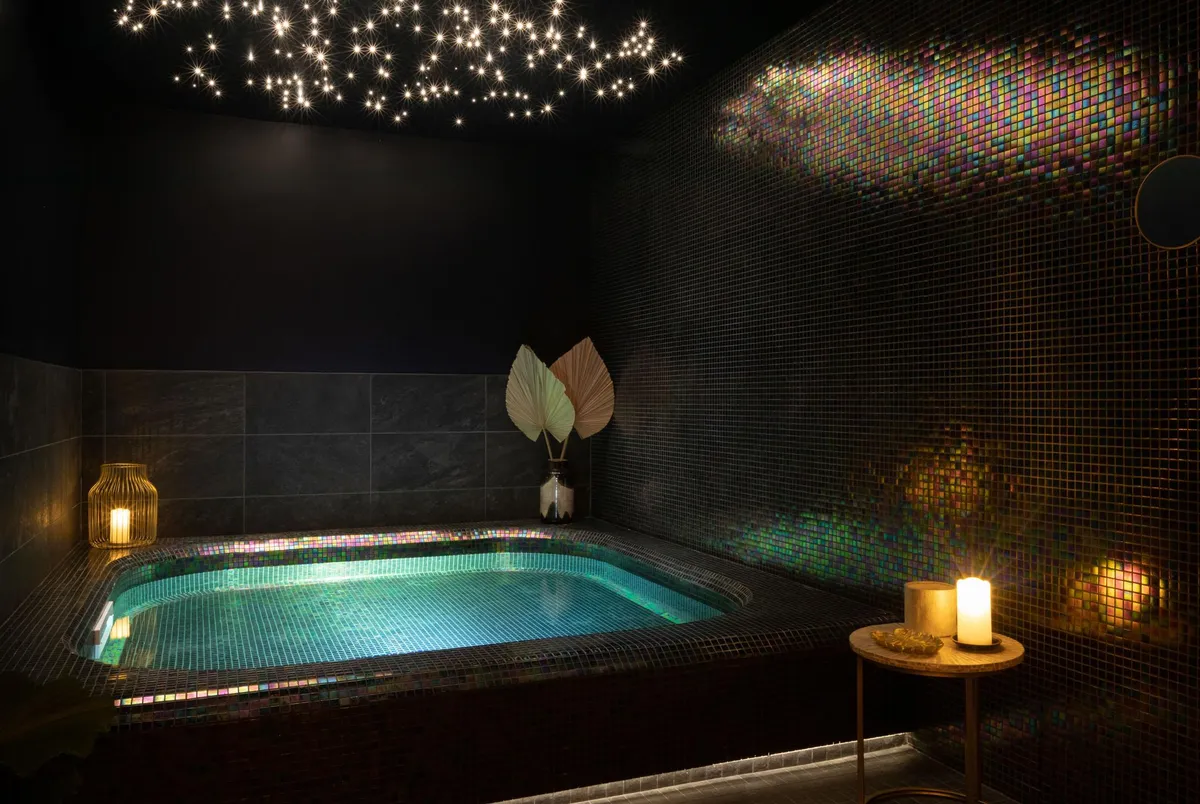 Beleuchtetes Hallenbad mit bunten Mosaiken an den Wänden und leuchtenden Sternen an der Decke