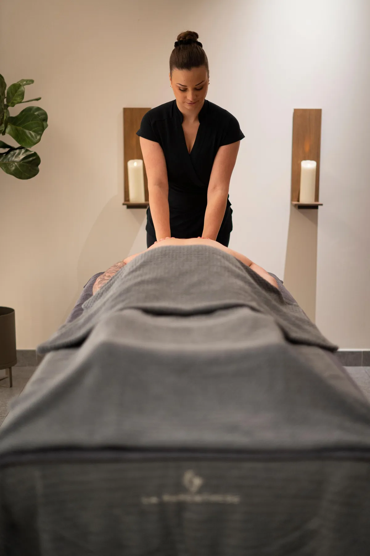 Eine Person führt eine Massage am Rücken einer Person durch, die auf einem mit einem Handtuch bedeckten Tisch liegt.