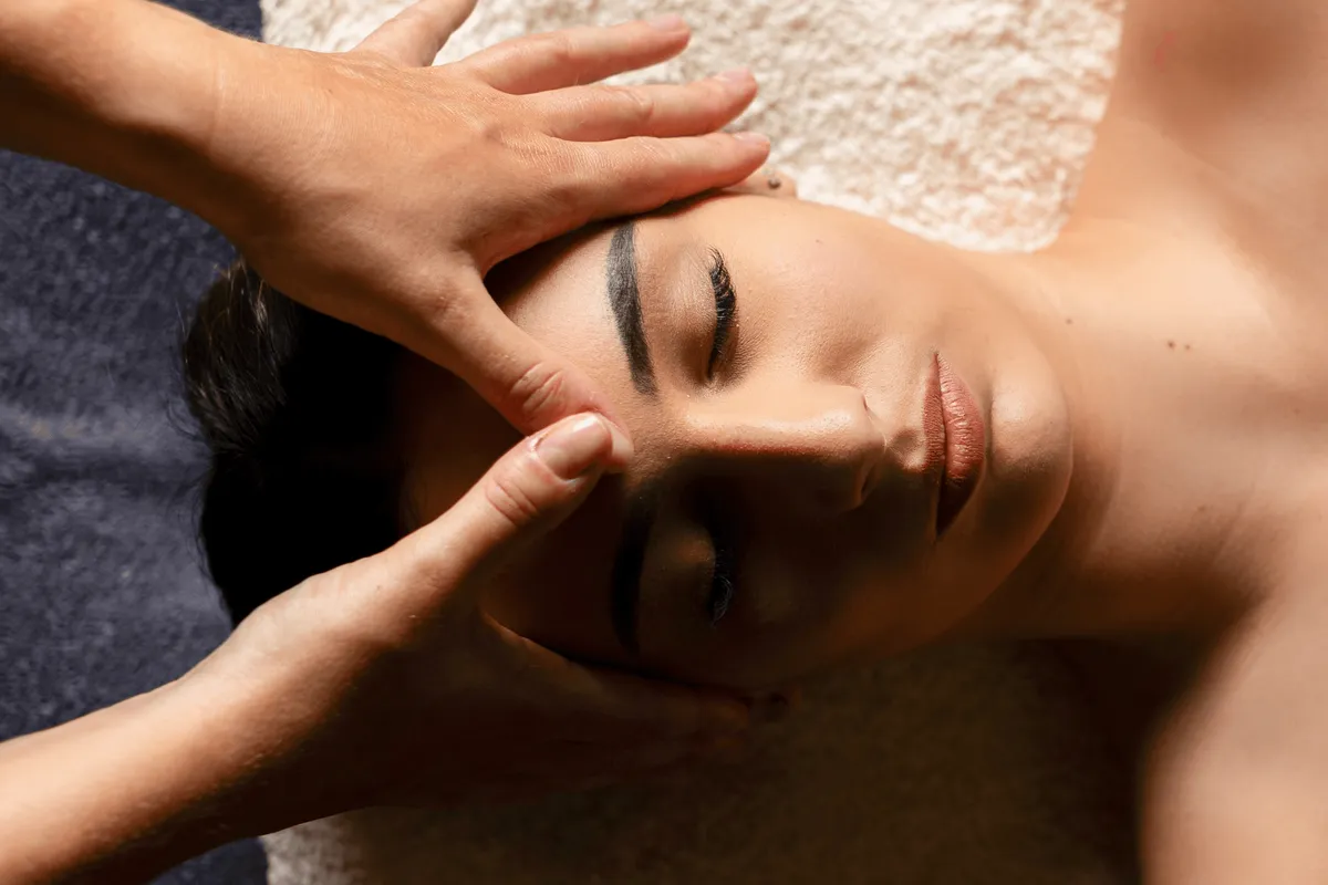 Une personne reçoit un massage facial avec les mains d'une autre personne visible