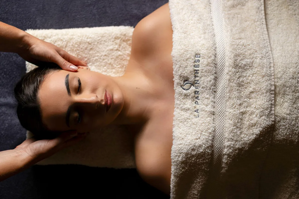Eine Person, die auf dem Bauch liegt, erhält eine Massage am Kopf, der mit einem Massagetuch bedeckt ist.