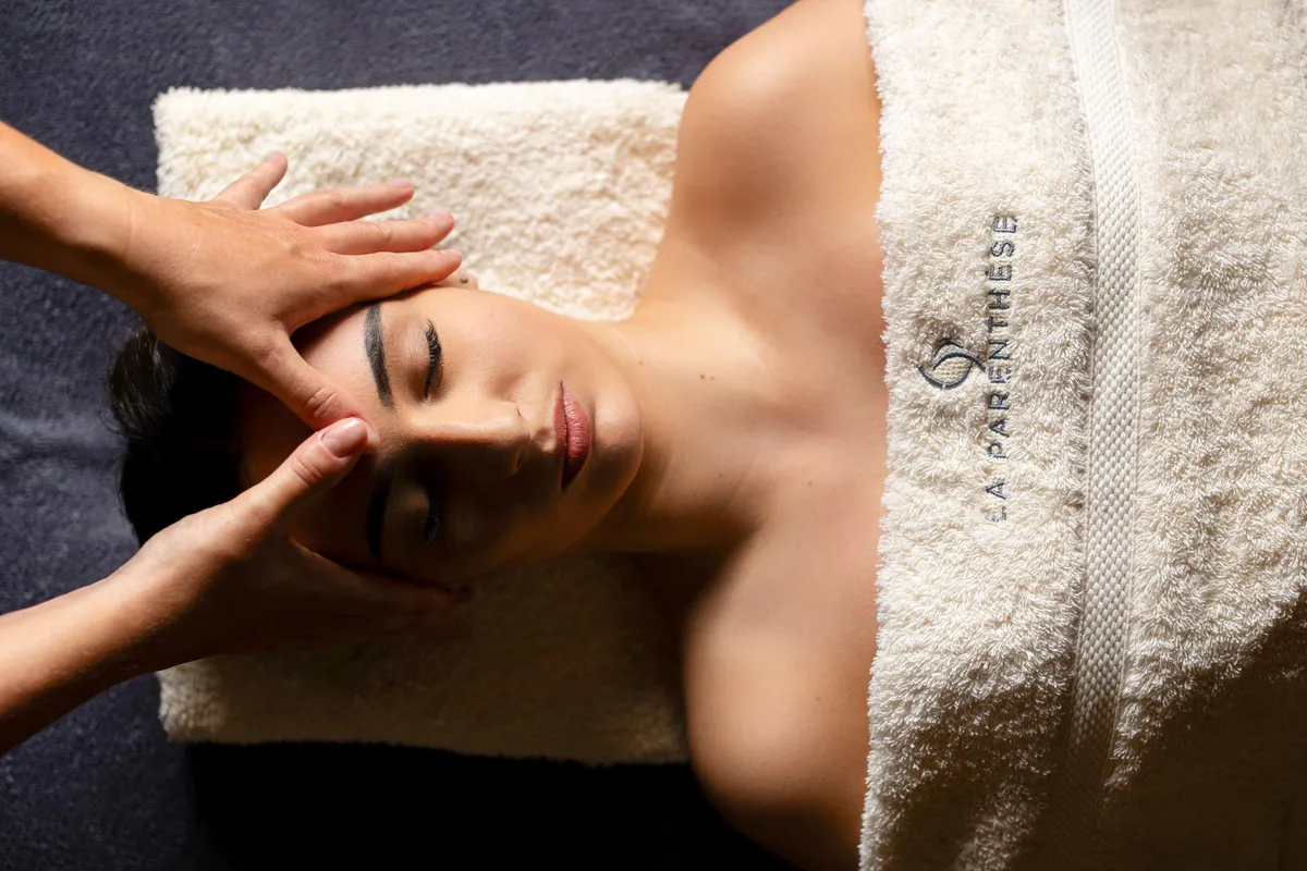 A person receives a facial massage, lying on their stomach, covered with a towel with an inscription.