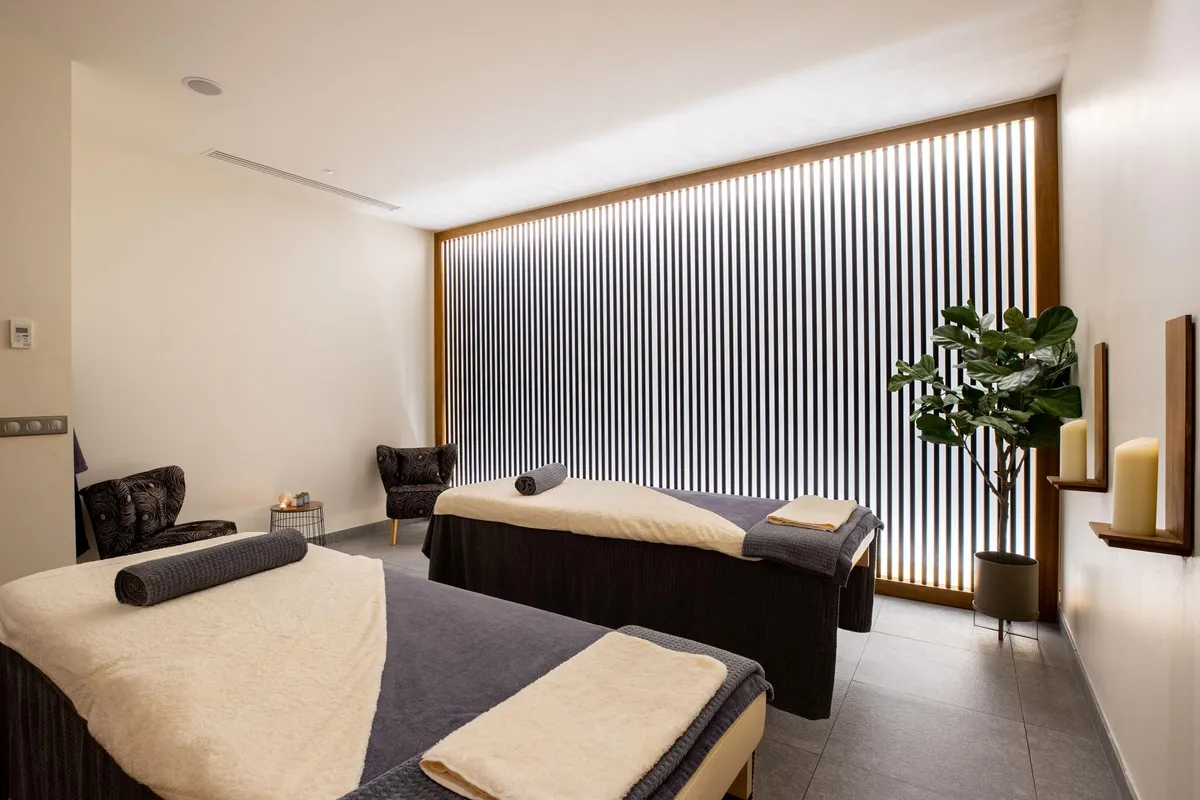 Salle de massage avec deux tables de massage, des serviettes, une plante et des chandelles