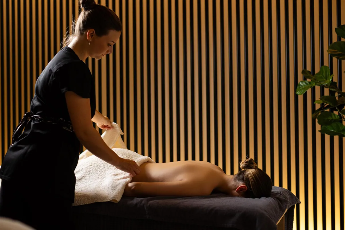 Une personne en tenue noire donne un massage à une autre personne allongée sur une table recouverte de serviettes