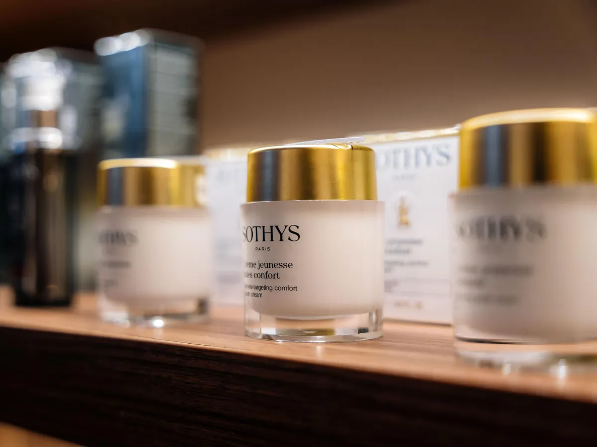 Plusieurs pots de crème cosmétique Sothys Paris avec des couvercles dorés sur une étagère en bois