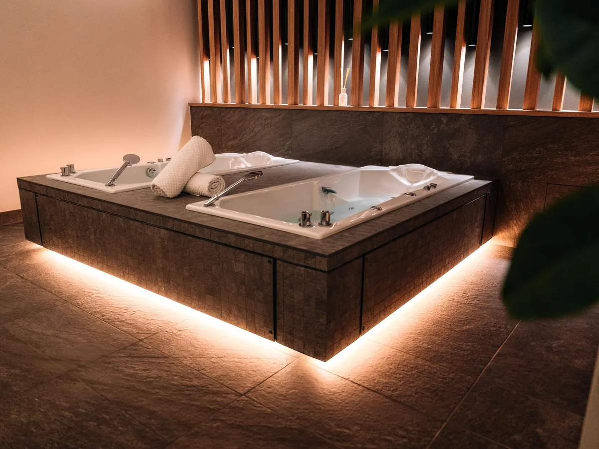 Whirlpool-Badewanne, in einen Steinmöbel eingebaut, mit LED-Bodenbeleuchtung und weißen Handtüchern am Rand