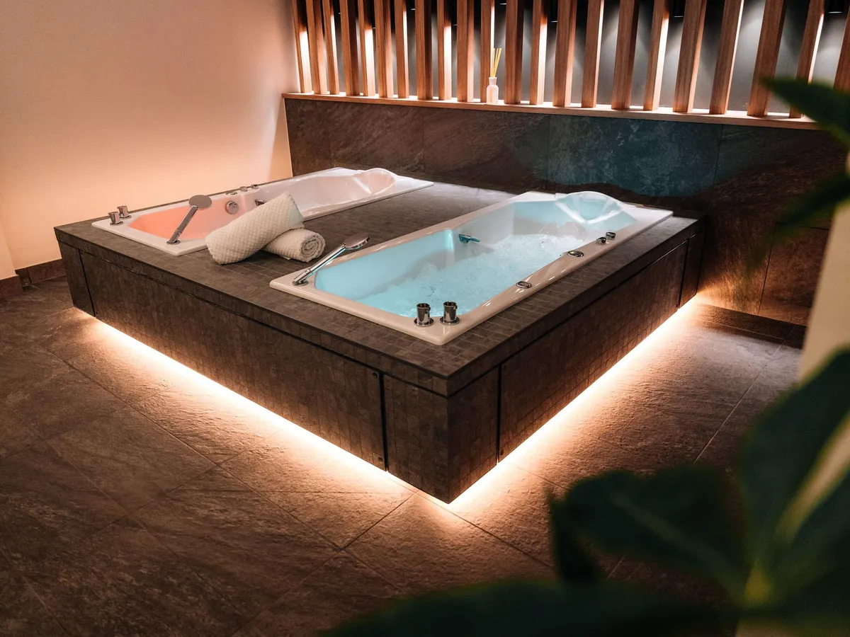 Große Whirlpool-Wanne, eingelassen in einen Steinrahmen, mit LED-Bodenbeleuchtung und Handtüchern am Rand
