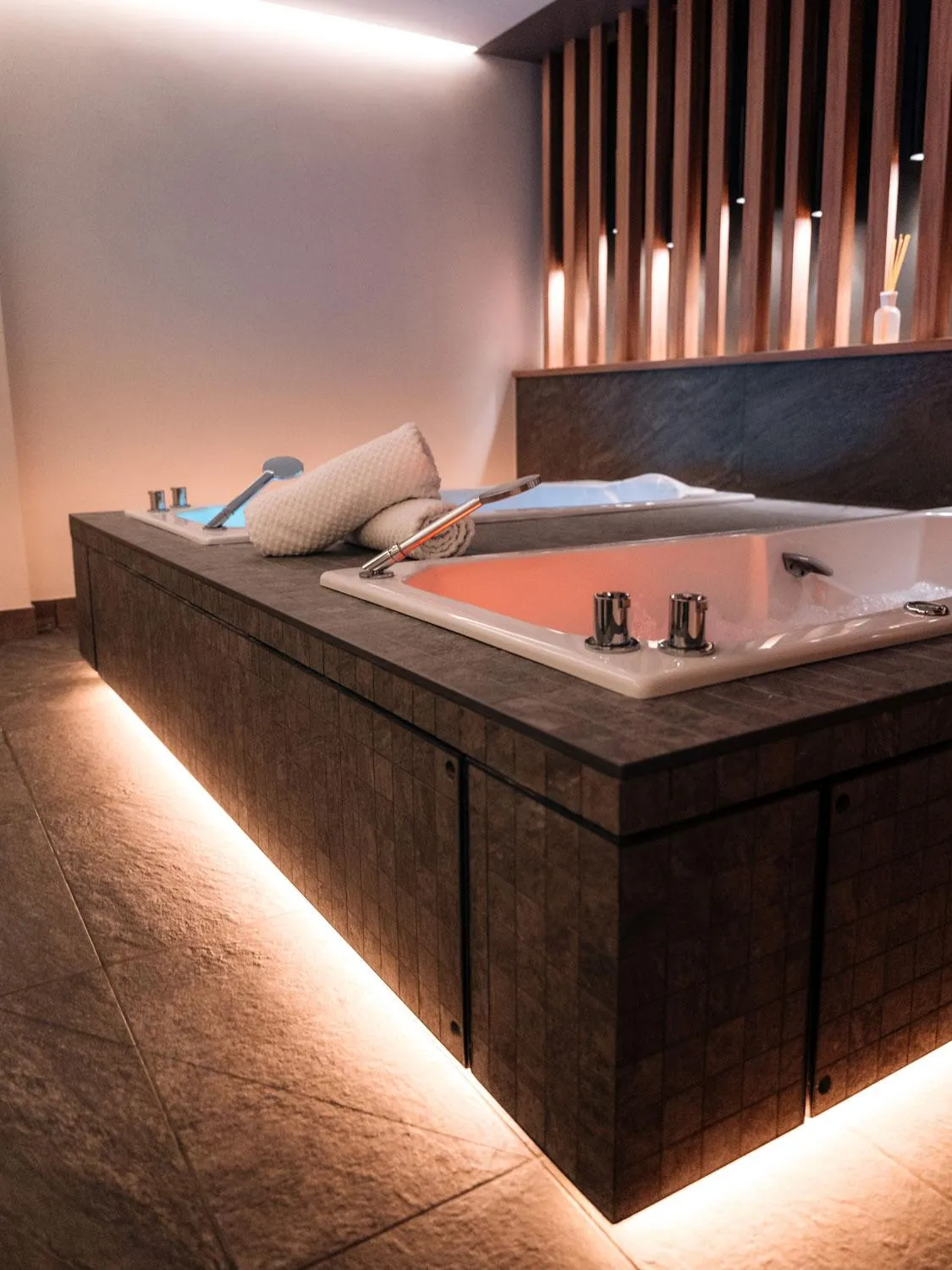 Eingebaute Badewanne mit LED-Lichtern unter dem Rand, Armaturen und einem Handtuch am Rand