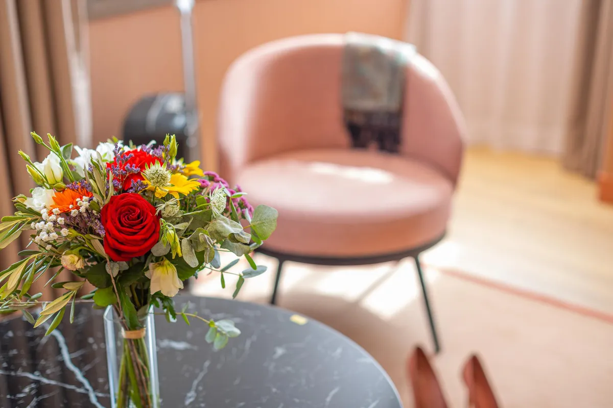 Ein Strauß bunter Blumen in einer transparenten Vase auf einem schwarzen Tisch mit Stühlen im Hintergrund