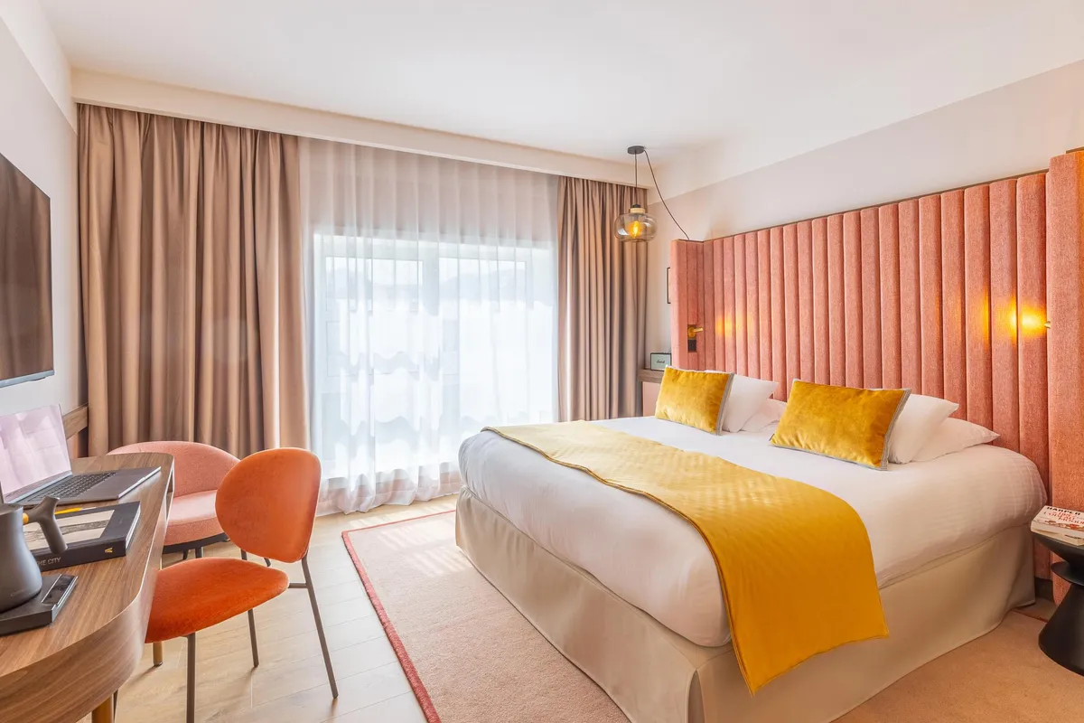 Chambre d'hôtel avec un lit double, deux chaises et un bureau près d'une fenêtre avec des rideaux