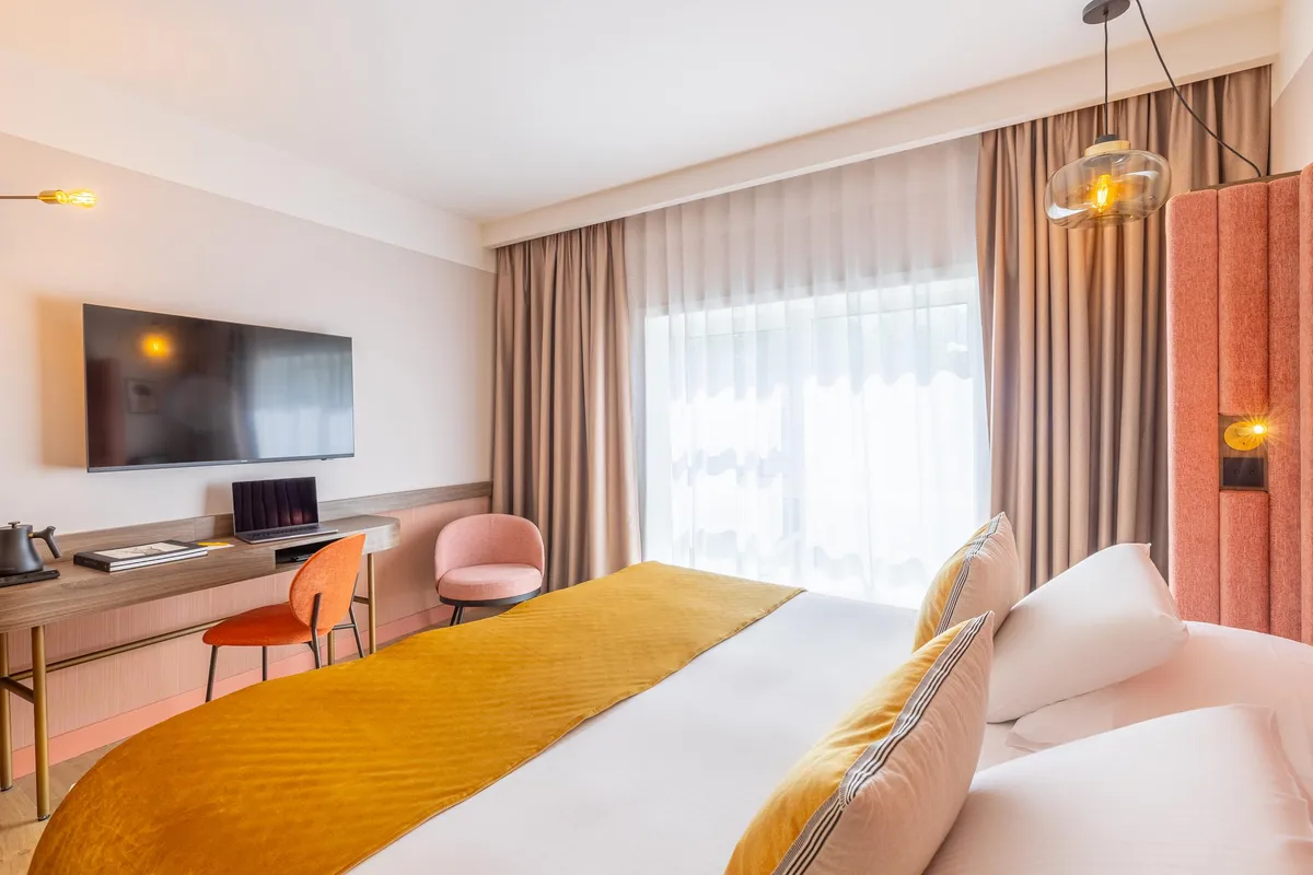 Moderne Hotelzimmer mit Doppelbett, Fernseher, Schreibtisch und einem großen Fenster mit Vorhängen