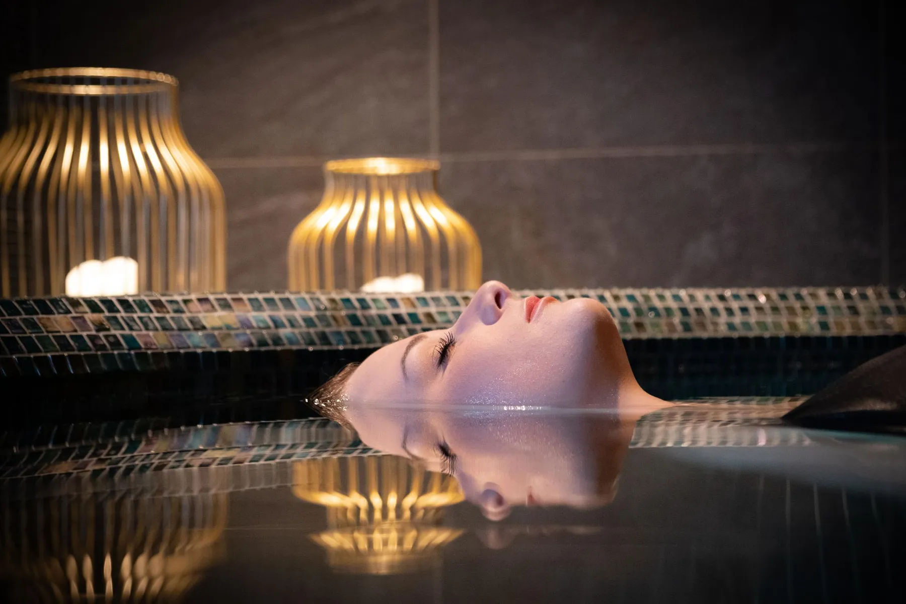 Une personne est allongée dans une piscine d'eau, la tête hors de l'eau, avec des lampes en arrière-plan