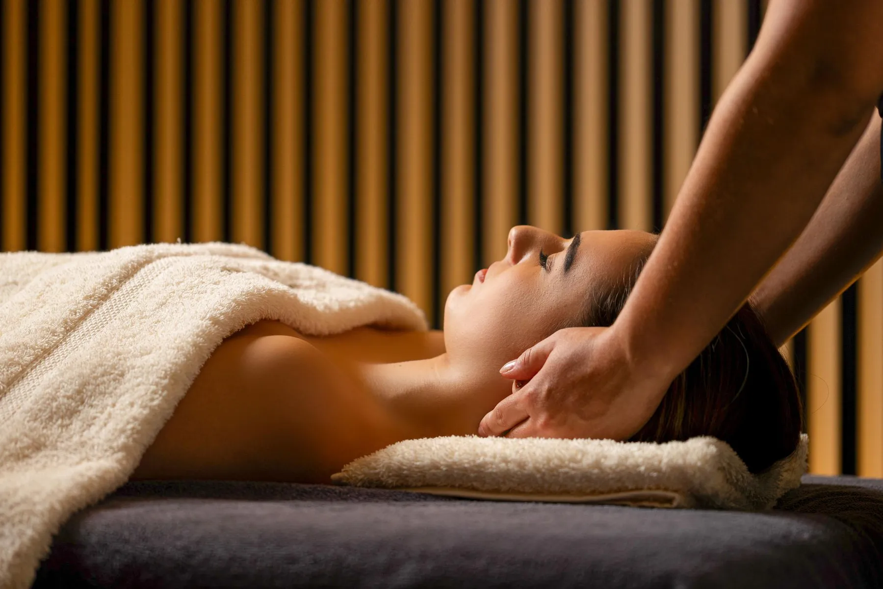 Une personne reçoit un massage sur un lit de massage recouvert de serviettes, dans une pièce aux murs à rayures verticales