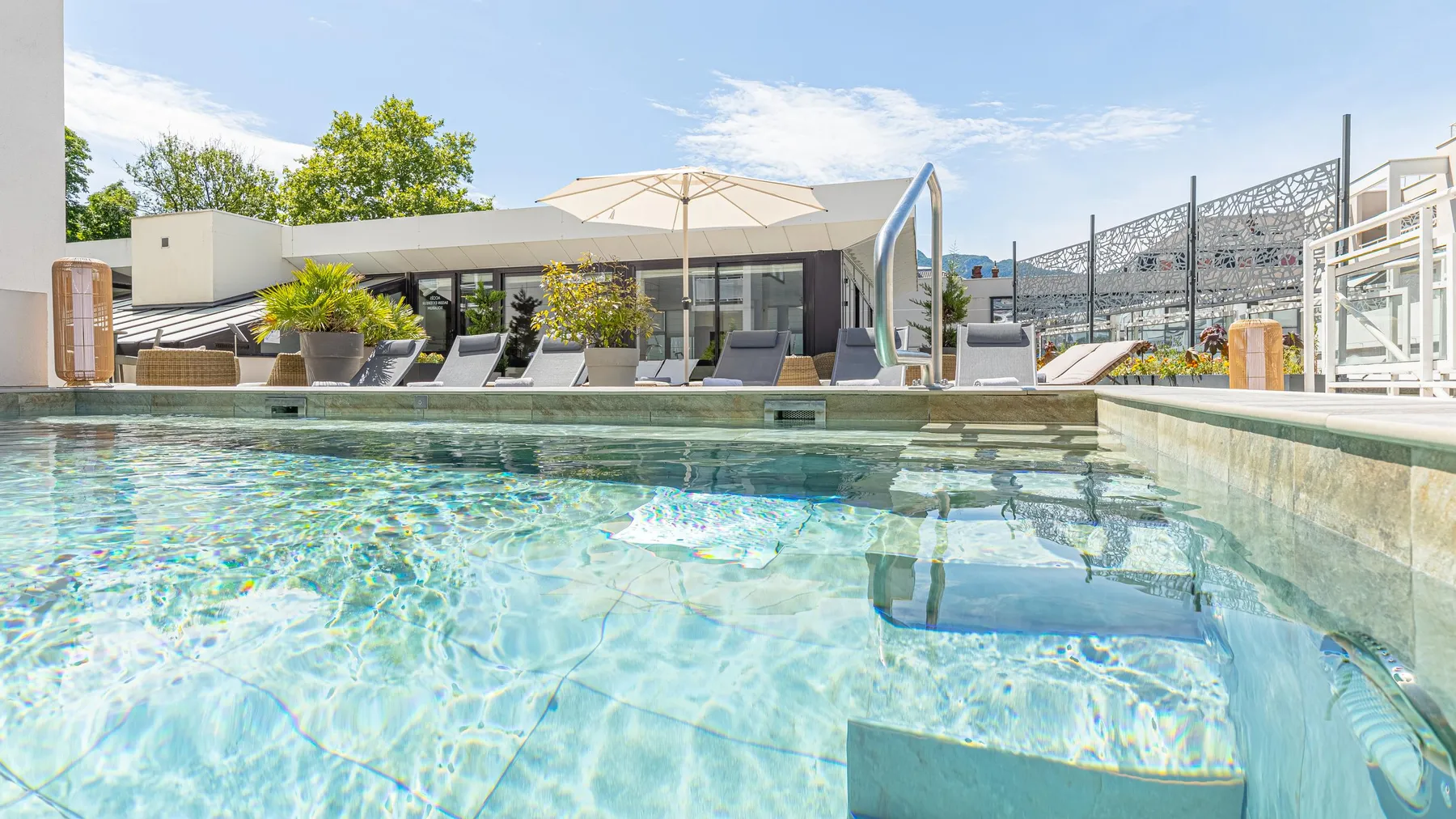 Piscine avec une vue sur un espace de détente extérieur comprenant des transats, des parasols et des plantes en pot