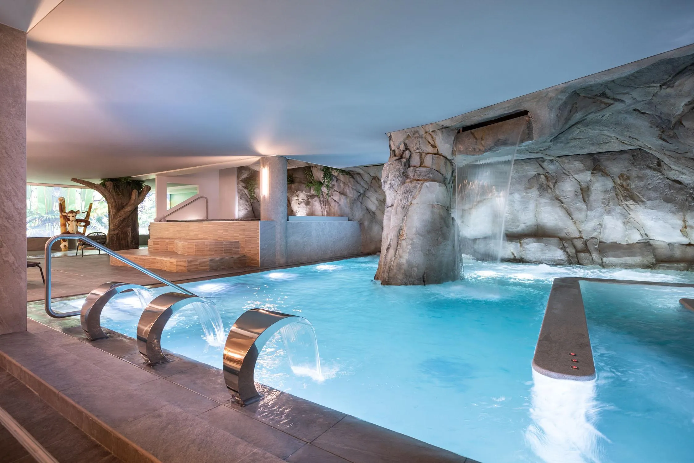 Piscine intérieure avec cascades et rochers artificiels, éclairée par une lumière naturelle et artificielle