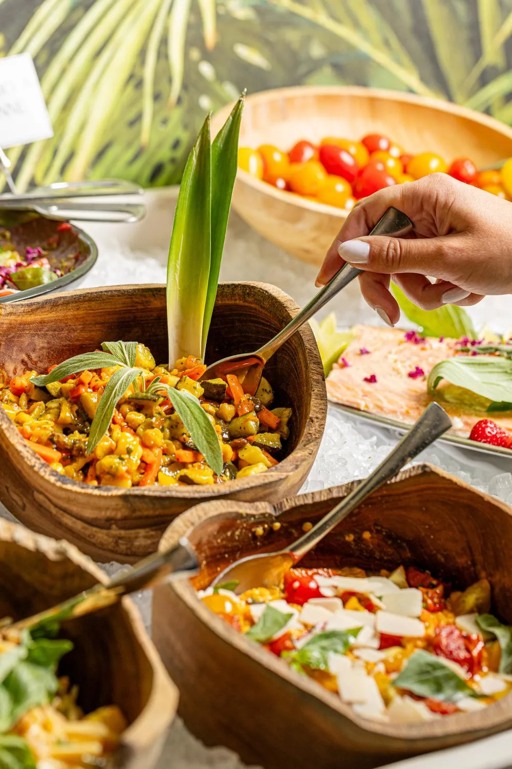 Une personne sert une préparation culinaire à base de légumes dans un bol en bois, entourée d'autres plats similaires