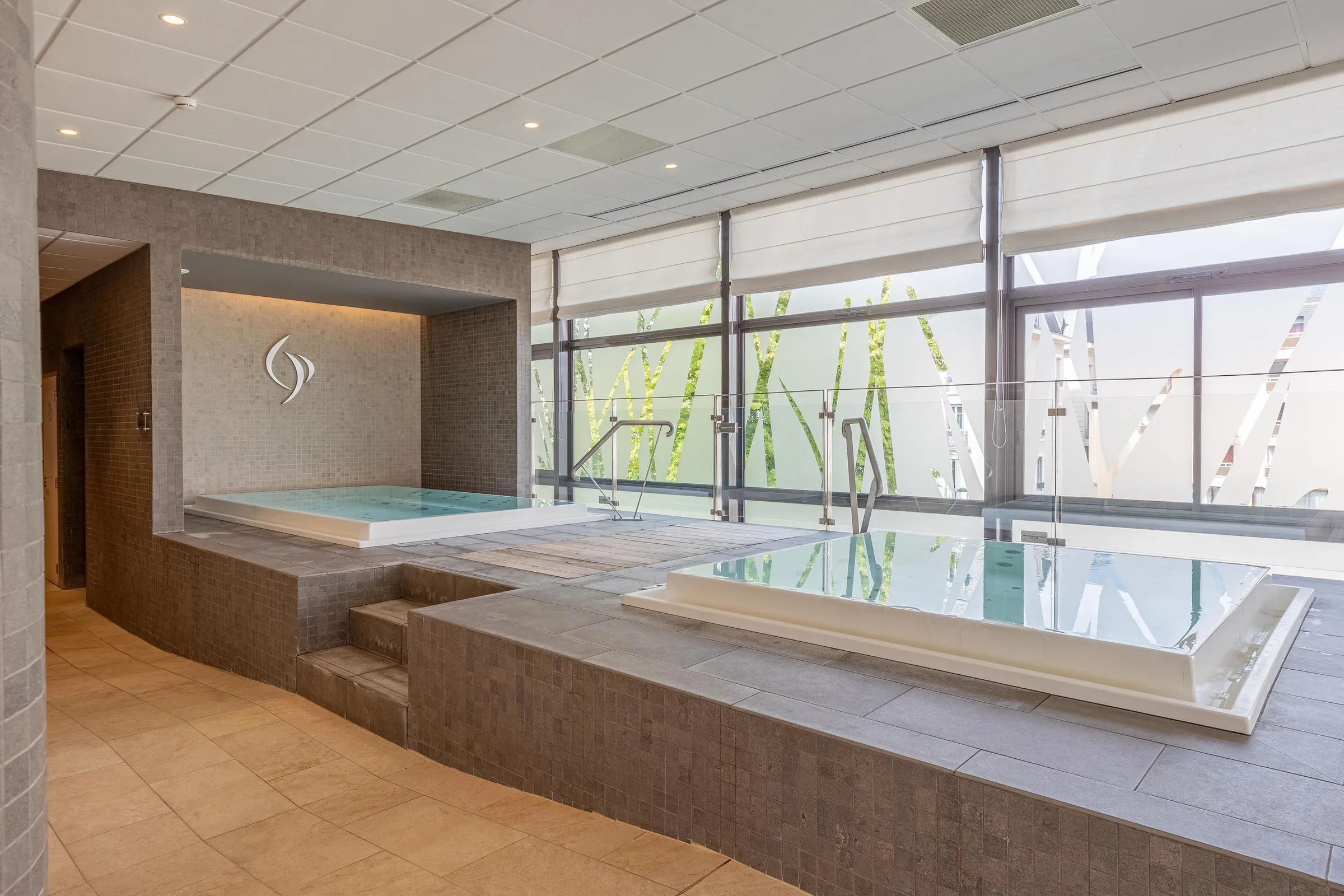 Spa room with two hot water pools and a large glass wall offering a view of an outdoor structure
