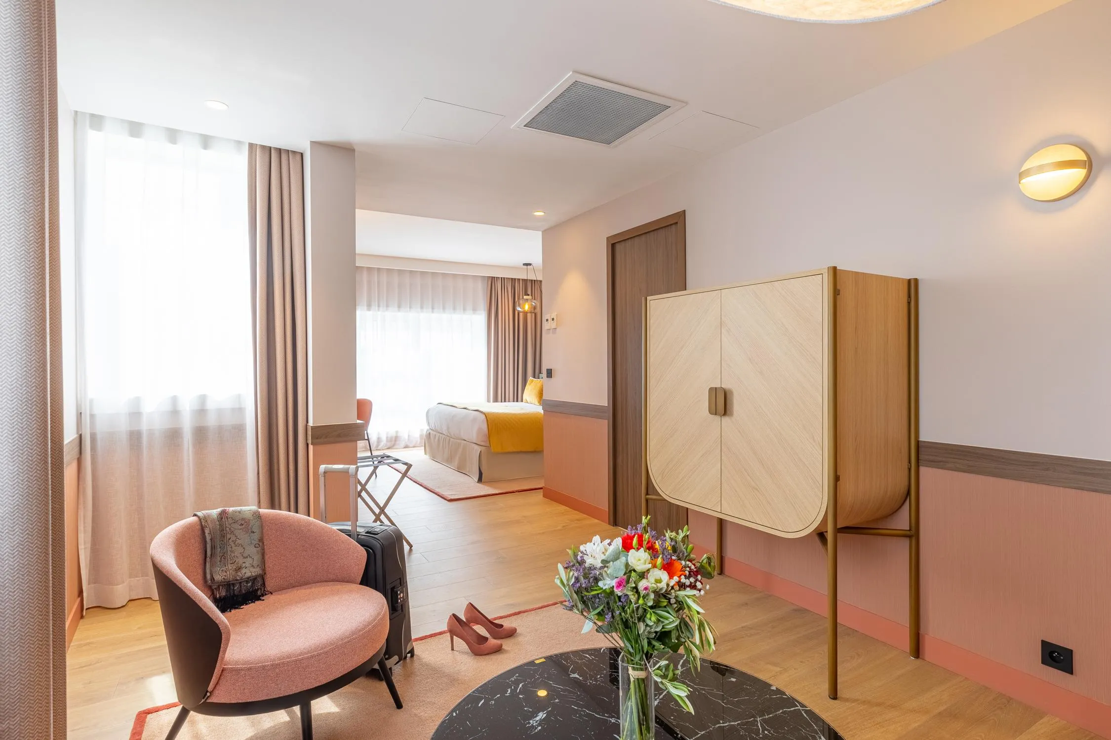 Chambre d'hôtel avec un fauteuil, une table basse, un vase de fleurs, un lit et une penderie