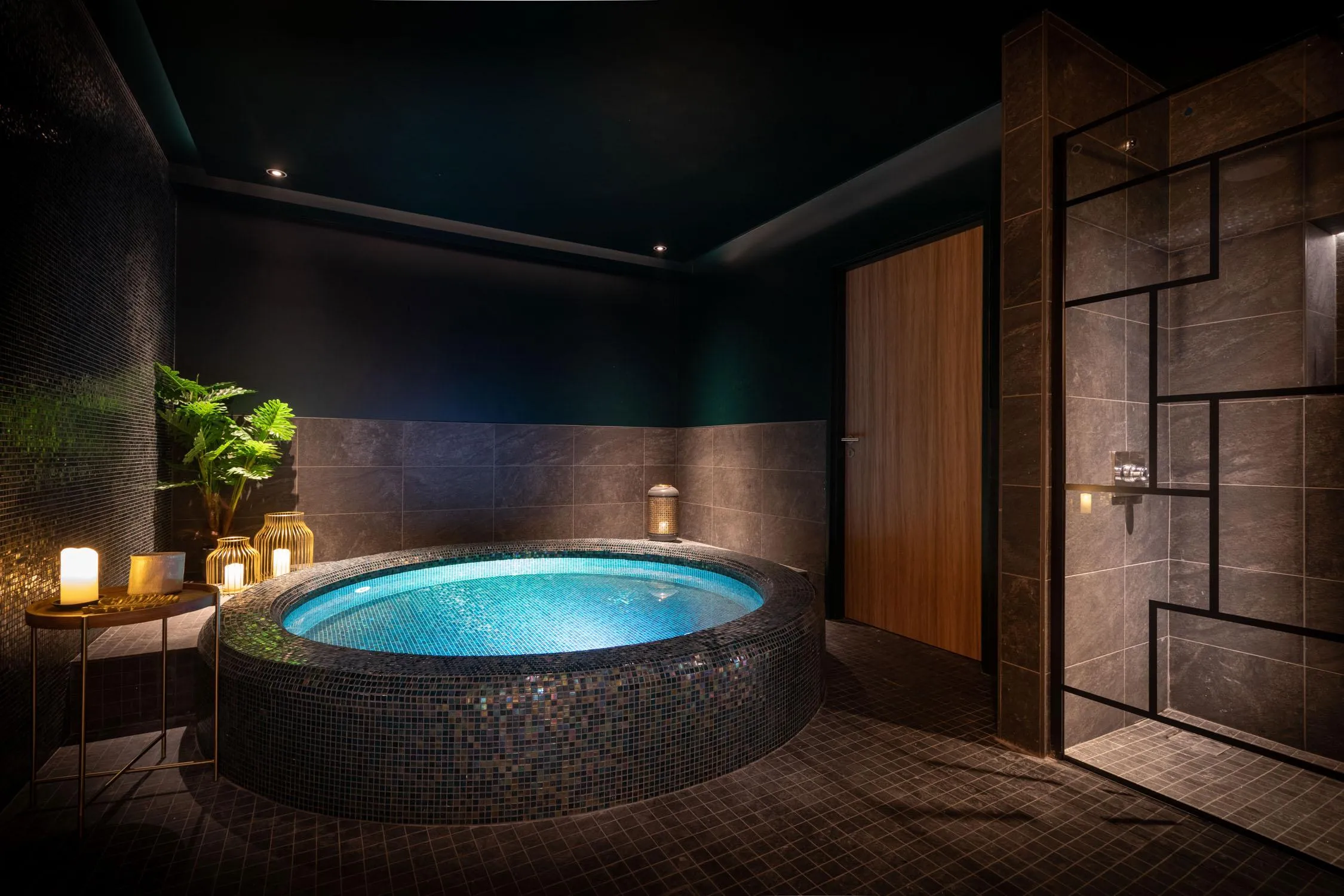 Salle de bain luxueuse avec un grand bain circulaire entouré de mosaïques, des bougies allumées sur une table et une plante verte